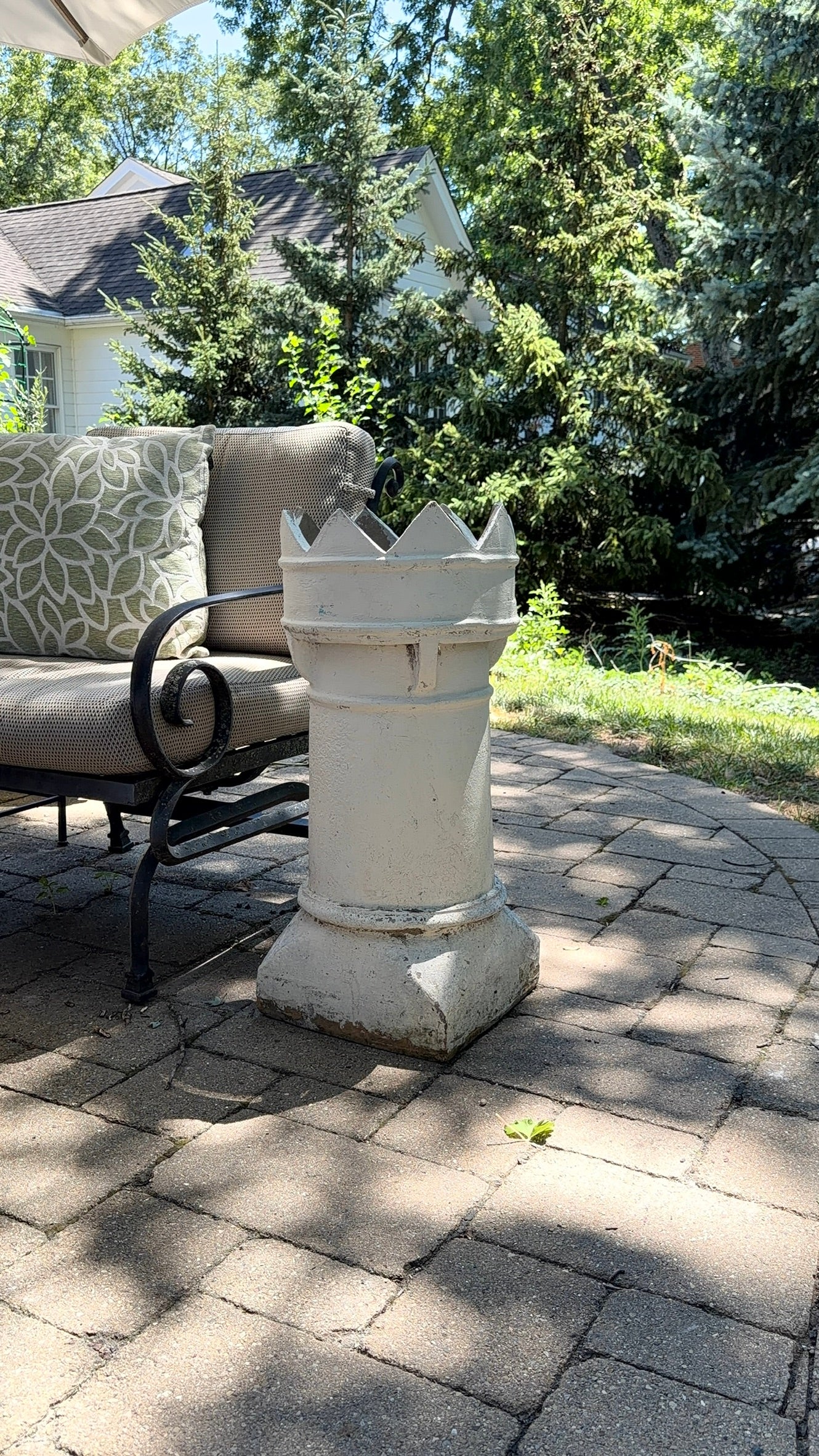 This is a vintage English crown chimney pot that has been painted white on a brick paver patio 