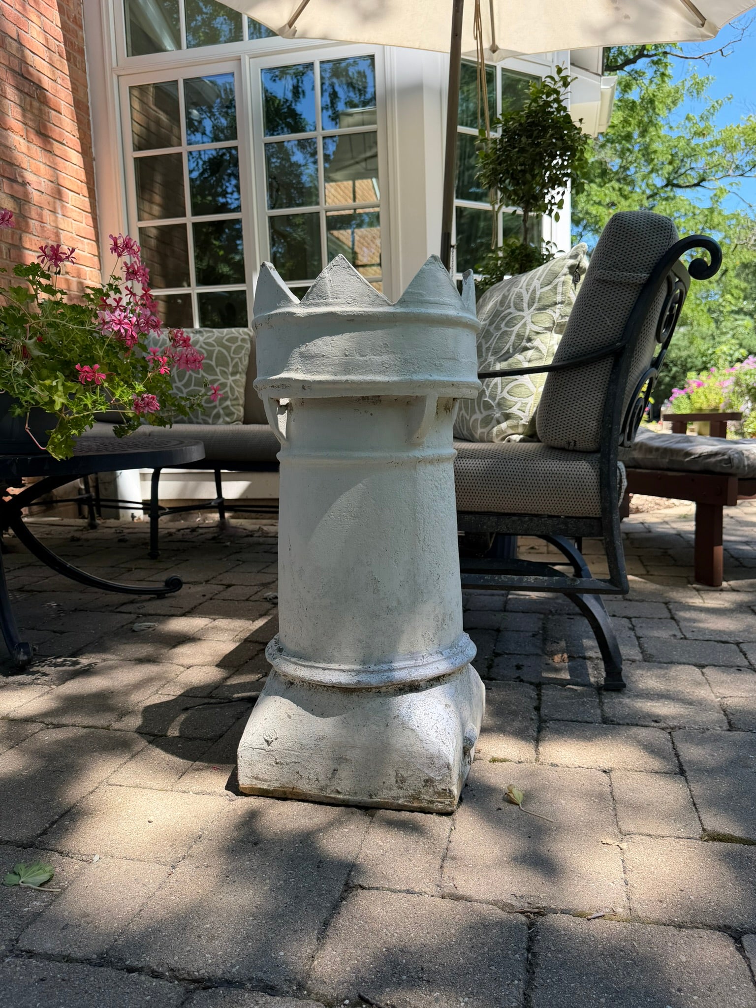 This is a vintage English crown chimney pot that has been painted white on a brick patio in backyard 
