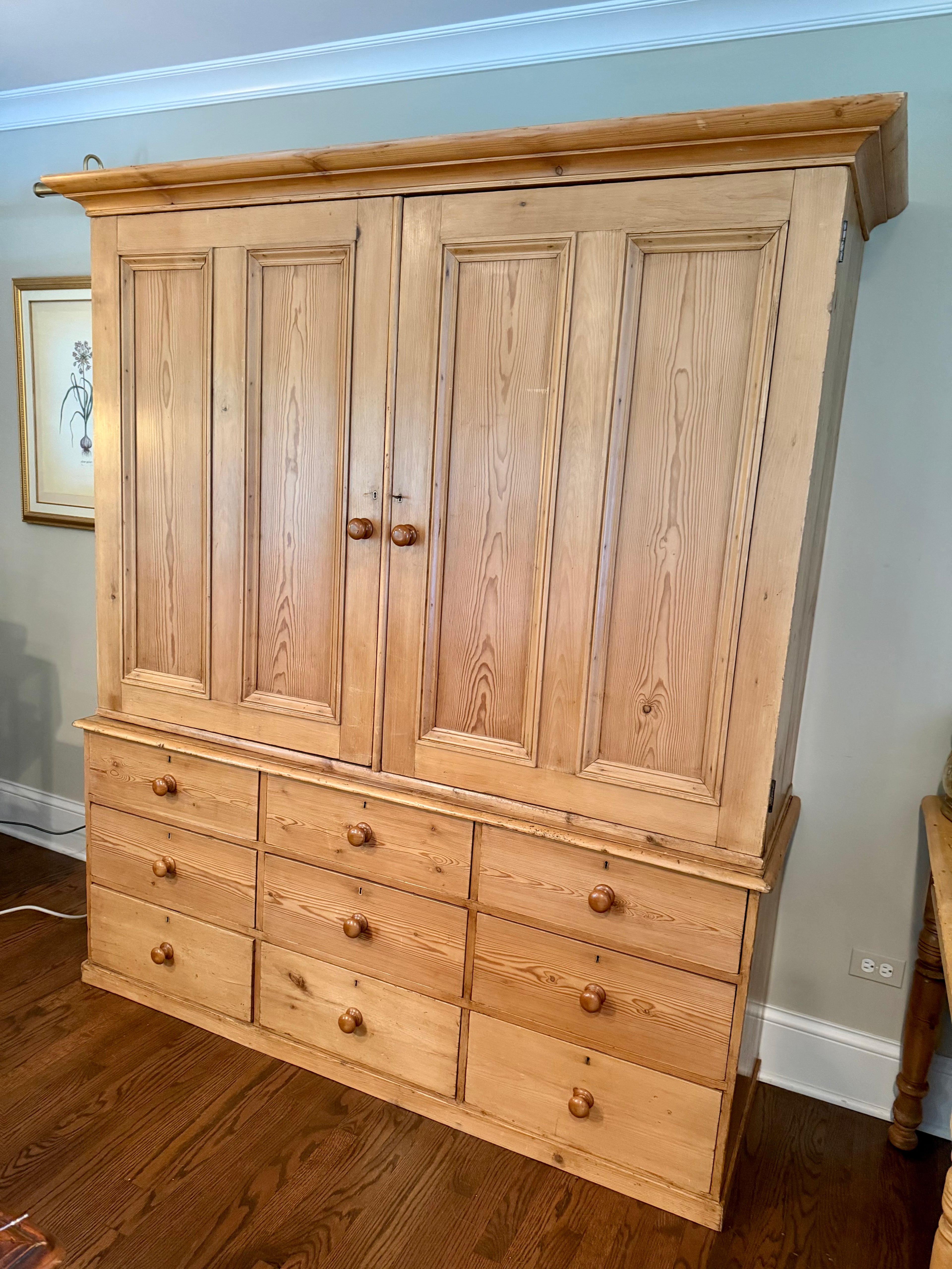 An authentic English Victorian pine Housemaid's Cupboard featuring two interior shelves, nine hand-dovetailed drawers, original pine knobs, and its original working key. A timeless antique linen press sourced from England.