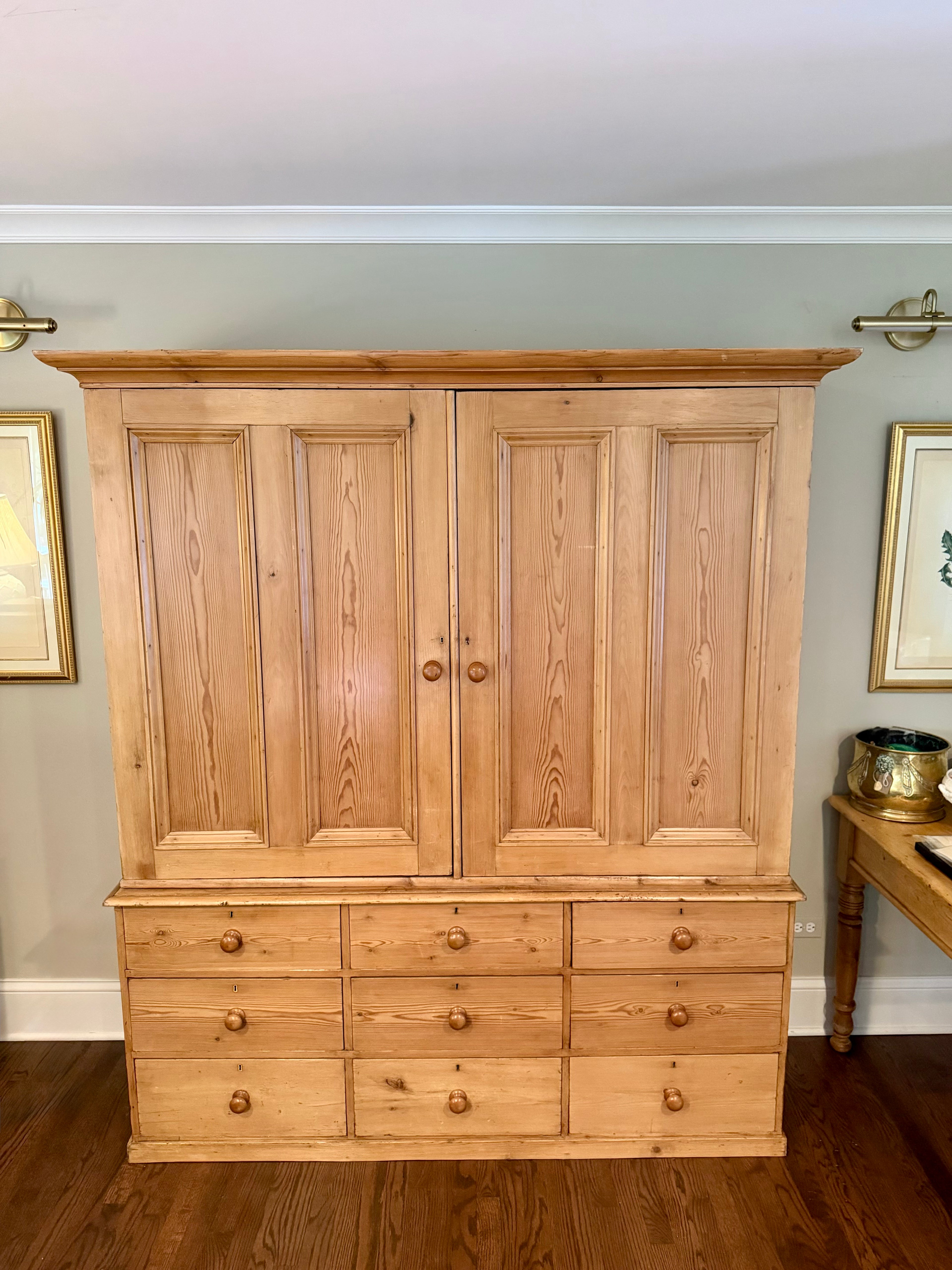 An authentic English Victorian pine Housemaid's Cupboard featuring two interior shelves, nine hand-dovetailed drawers, original pine knobs, and its original working key. A timeless antique linen press sourced from England.