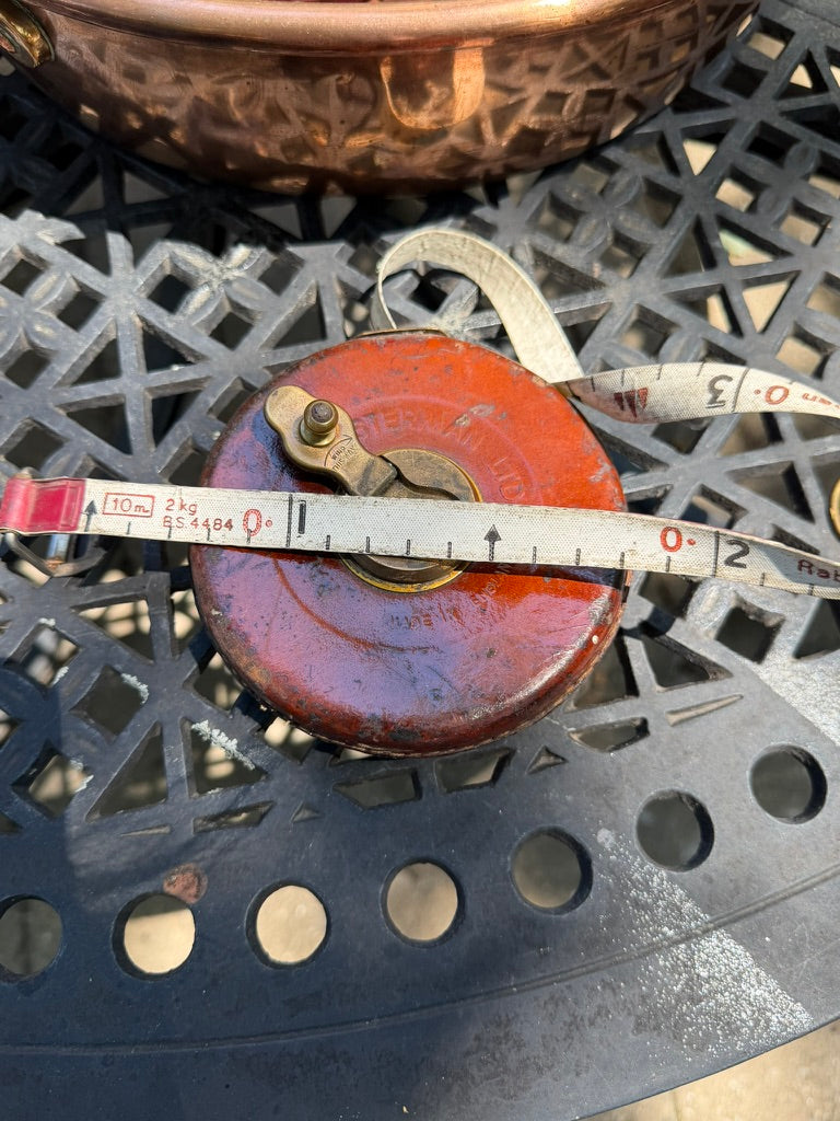 A close-up of a vintage leather  measuring device with a metal tape measure draped across it, placed on a black metal patio table.