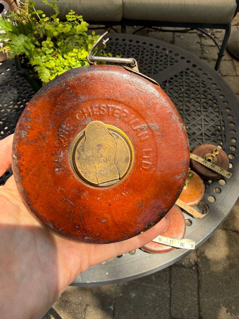 A hand holding a round, vintage red metal bellows with a brass and leather with embossed brand name Chesterman, Ltd.